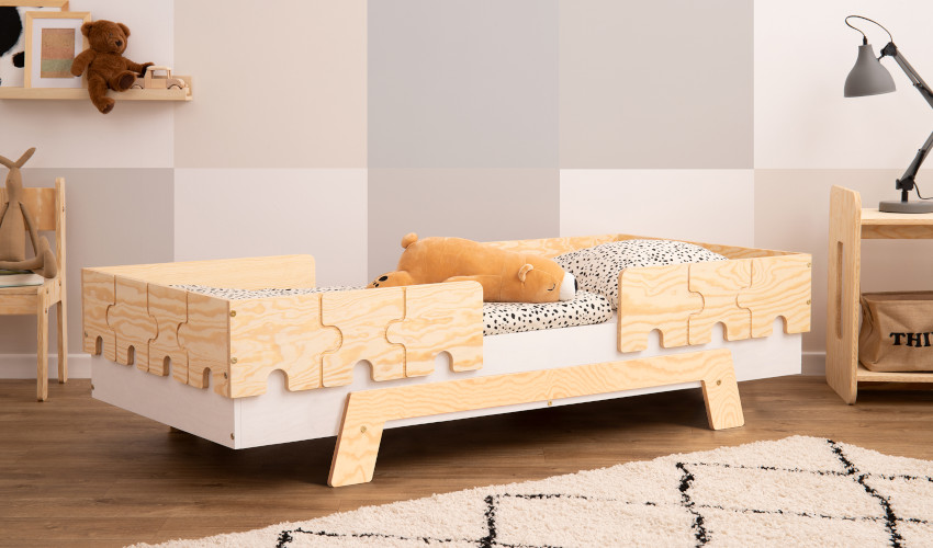Białe drewniane łóżko z barierkami w kształcie puzzli wykonaną ze sklejki sosnowej w kolorze naturalnego drewna